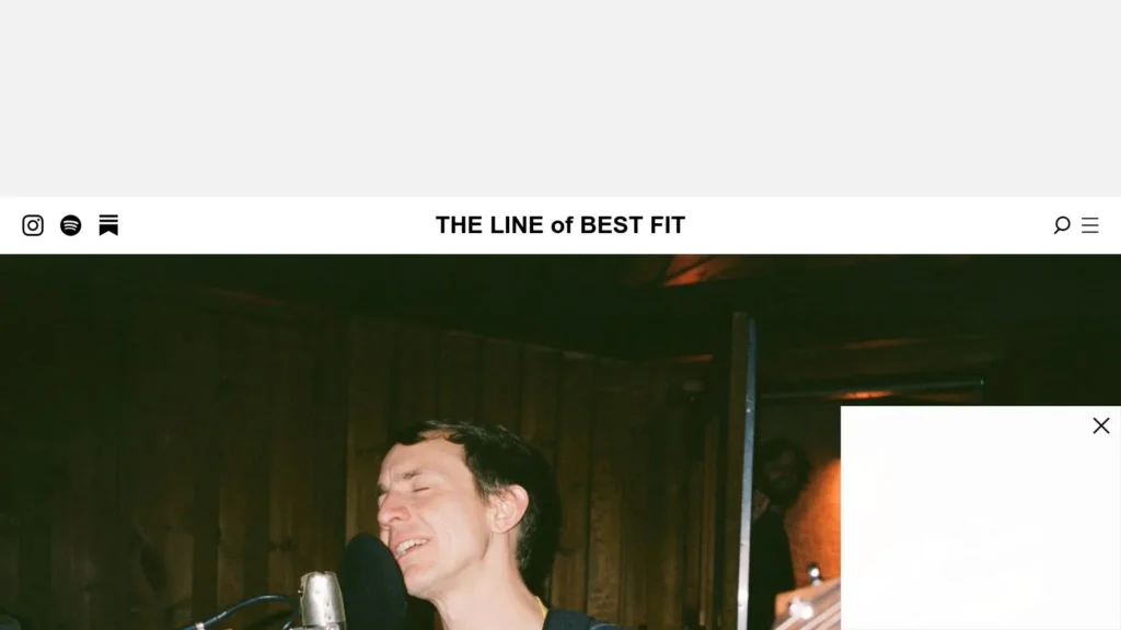 The Line of Best Fit music site homepage with singer performing live under warm stage lighting