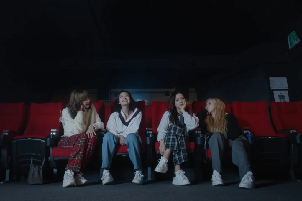 Four women sitting in red theater seats, chatting and smiling in a dimly lit cinema.