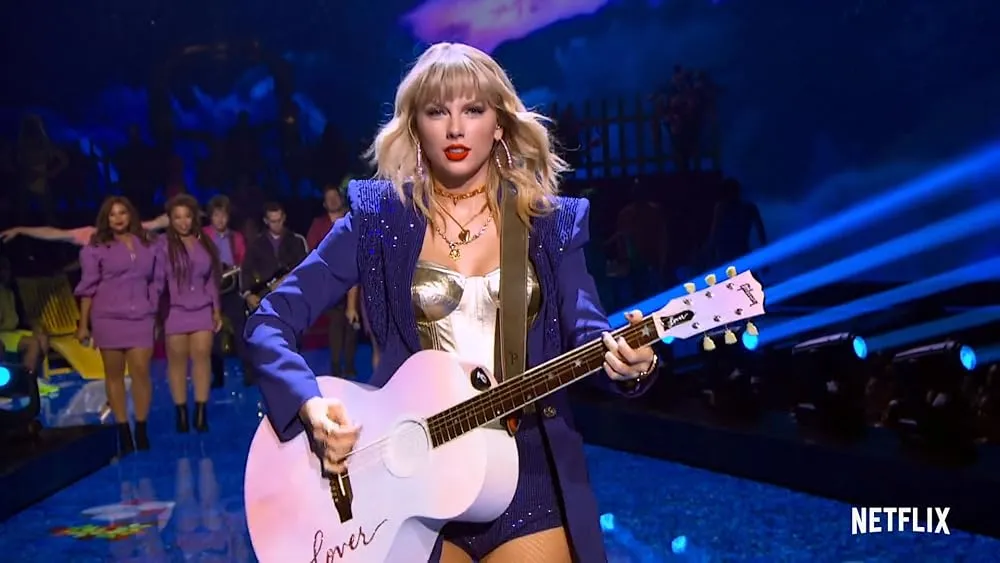 Singer performing onstage with a pink guitar under blue lights during a live concert performance.