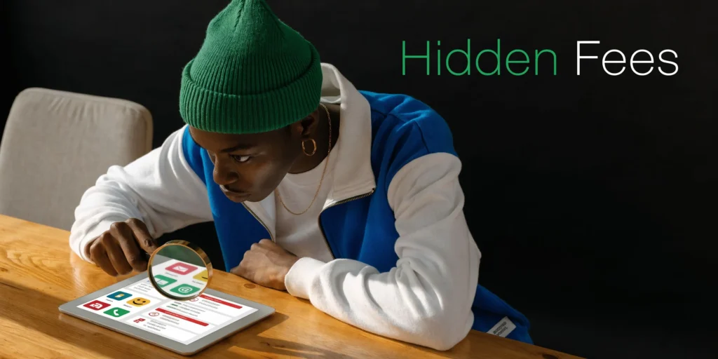 Person examining a tablet with a magnifying glass beside “Hidden Fees” text at a wooden table.