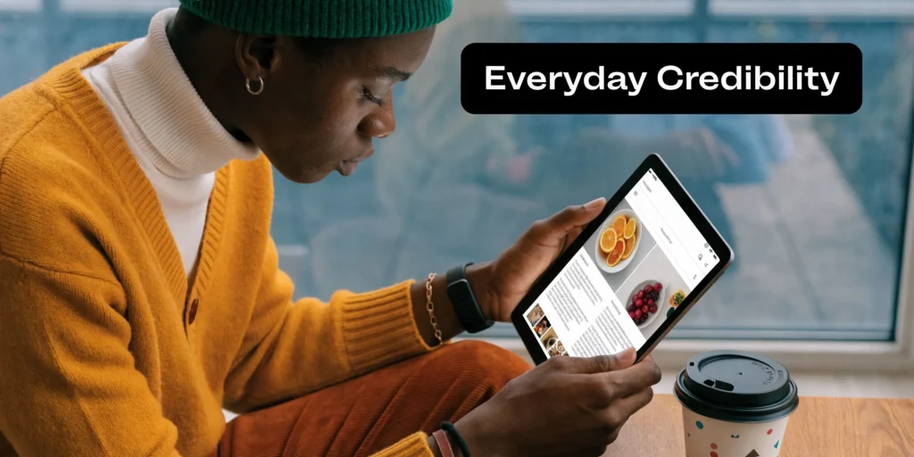 Person reading articles on a tablet beside “Everyday Credibility” text while sitting by a window.