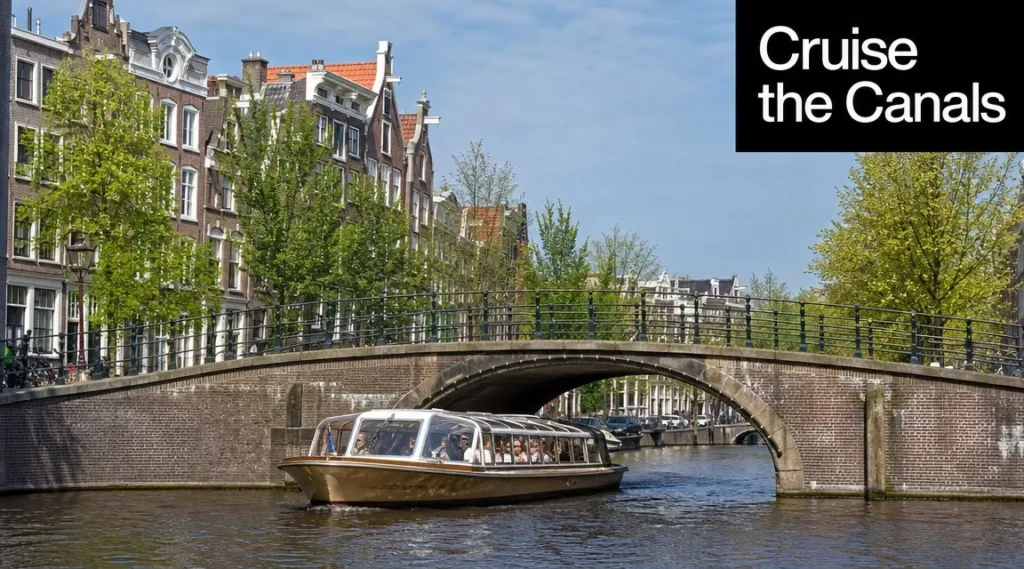 What to Do in Amsterdam: 10 Unmissable Experiences Canal tour boat passing under a historic bridge in Amsterdam, lined with classic canal houses and trees.