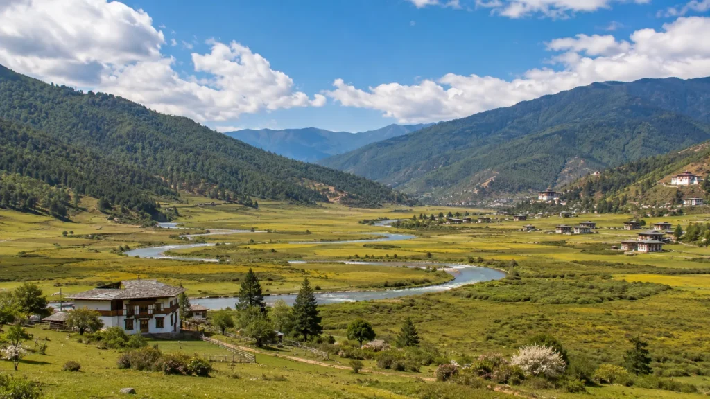Bhutan’s Phobjikha Valley with winding river, green meadows, traditional homes, and forested mountains under a blue sky.