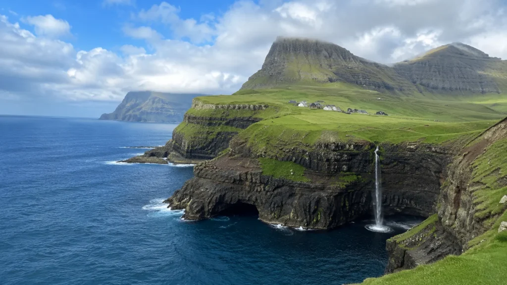 Faroe Islands landscape with dramatic green cliffs, a coastal waterfall, rugged mountains, and deep blue Atlantic waters.