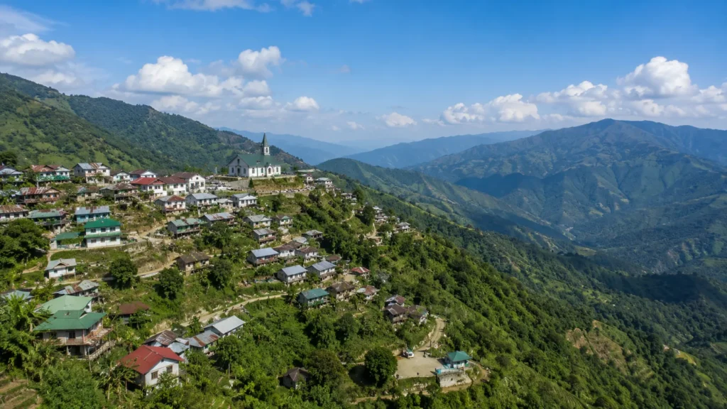 Nagaland mountain village in India with hillside homes, a church, lush green valleys, and distant mountains under a blue sky.